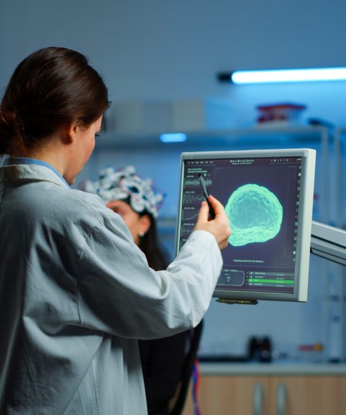 Researcher looking at monitor analysing brain scan while coworker discussing with patient in background about side effects, mind functions, nervous system, tomography scan working in laboratory