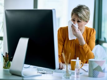 Sick businesswoman blowing nose while working on a computer in the office.