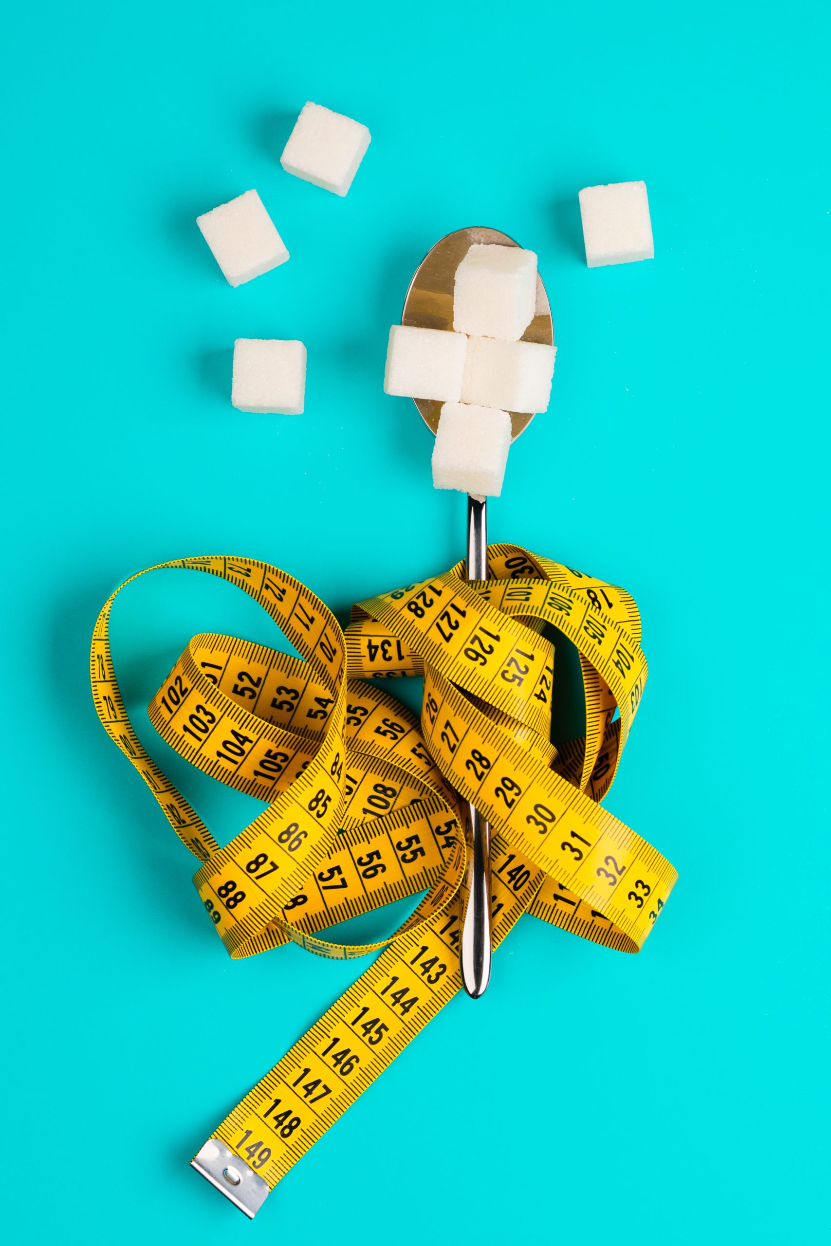 Sugar-replacing tablets or sugar with a spoon are entangled in the measuring tape. On a blue background. The concept of diabetes and proper nutrition.